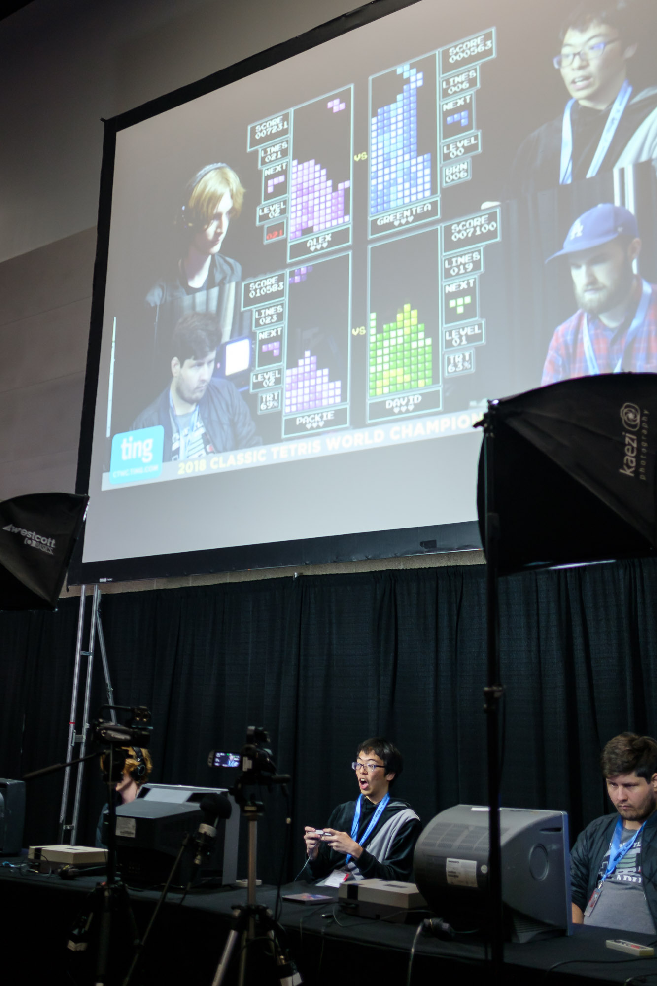The main stage at CTWC in 2018 with a big projector screen in the back. Players Kitaru, Greentea, and Pacike can be seen playing behind CRT monitors.