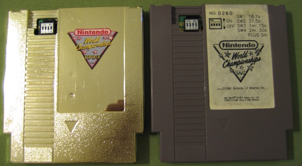 Two NES game cartridges laying side by side, the first one is a gold version of the NWC 1990 game, and the second is the gray version of the same game.
