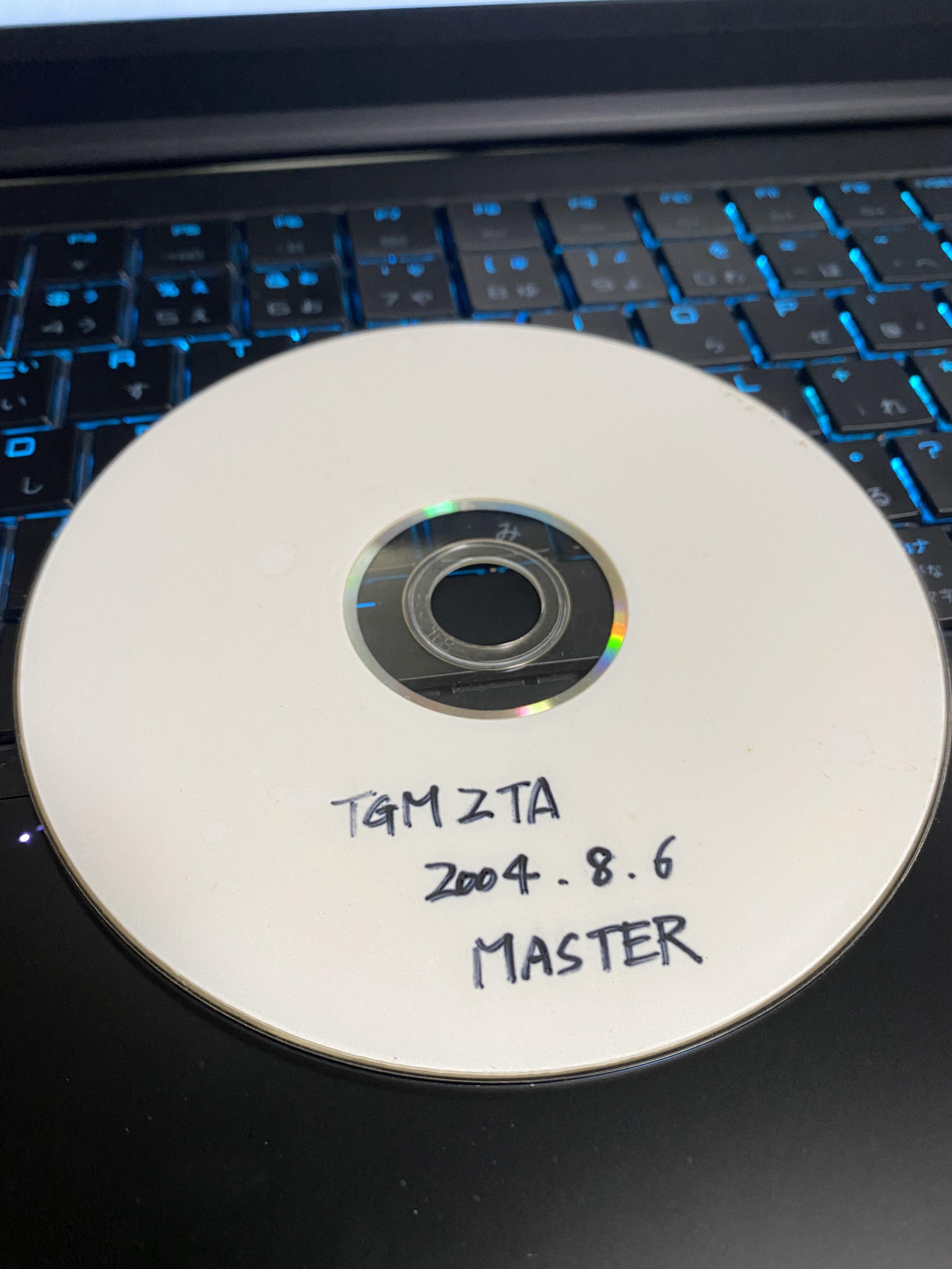 A photo of a CD-RW with a hand written text on it saying: 'TGM2TA 2004.8.6 MASTER'.